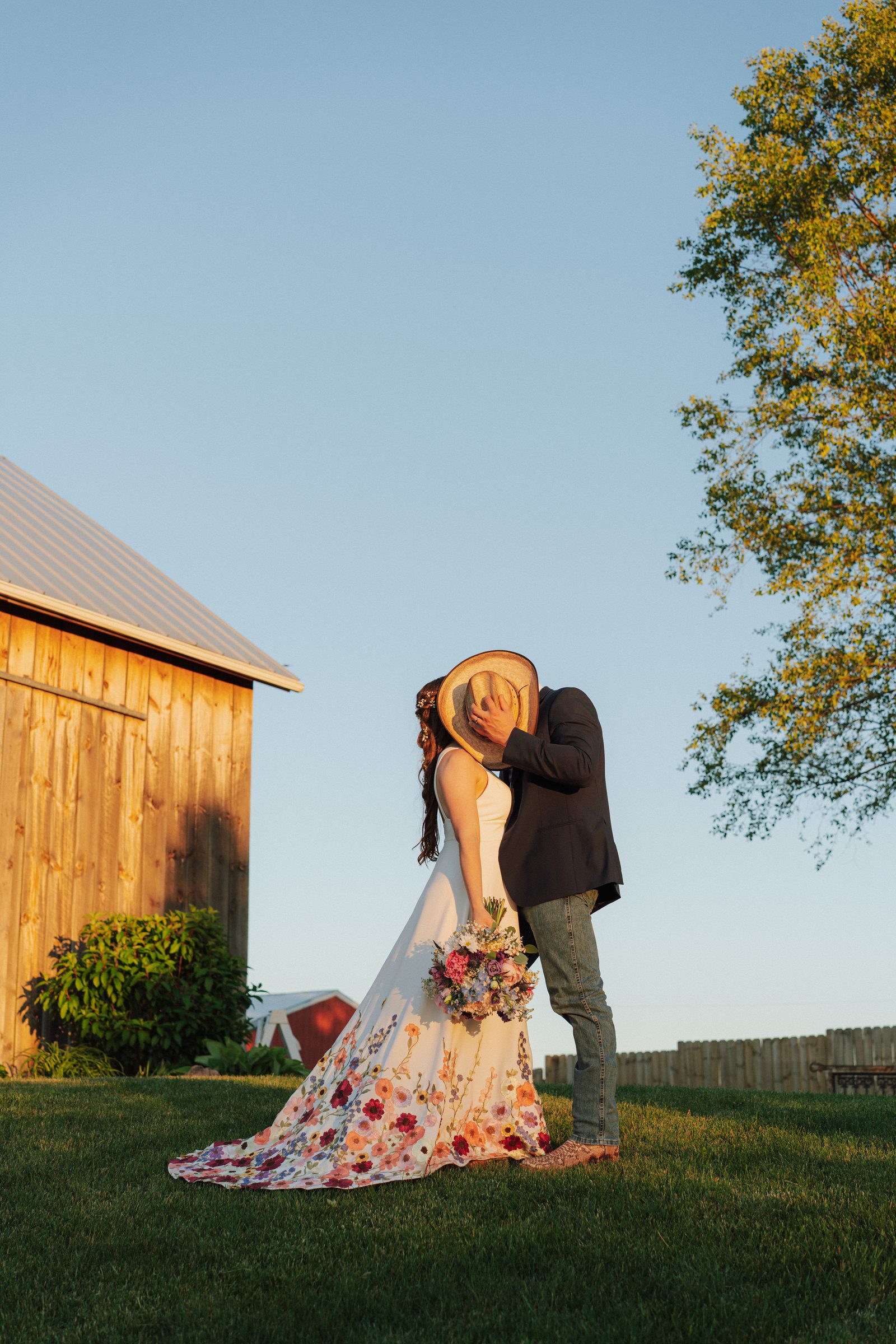 Couple kissing beneath a cowboy hat beside the barn at Ridge View Ranch