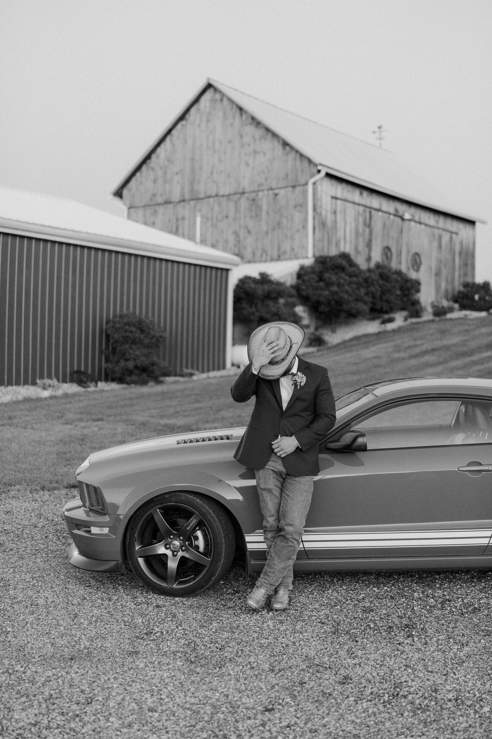 Groom beside a classic Mustang in front of the barn at Ridge View Ranch